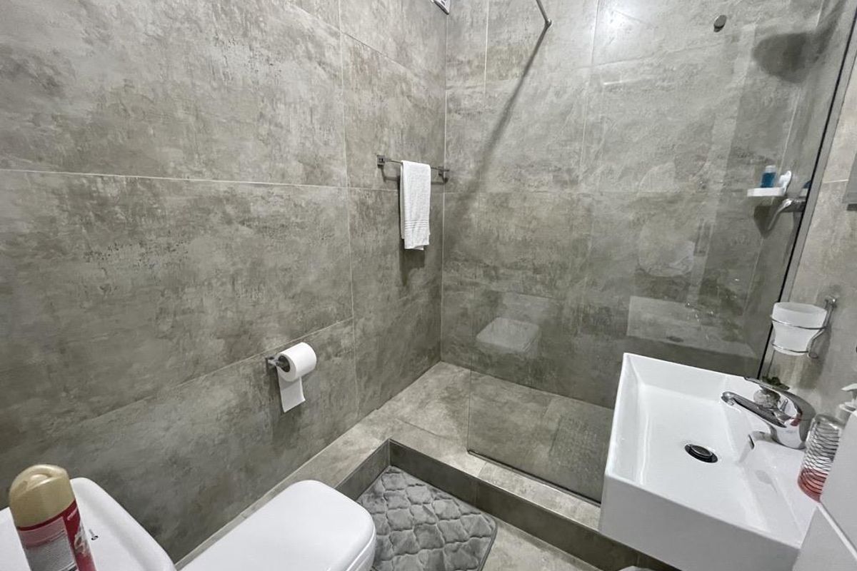 Modern bathroom featuring large-format grey wall tiles, a walk-in shower with a glass screen, a wall-mounted basin, and a toilet.