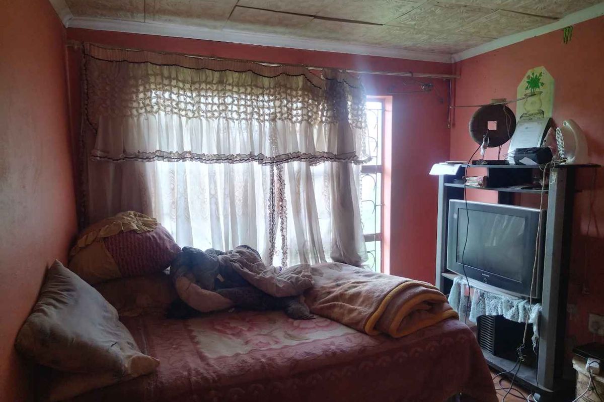 A bedroom featuring a window with security bars, textured ceiling tiles, and painted walls, providing a functional sleeping space.