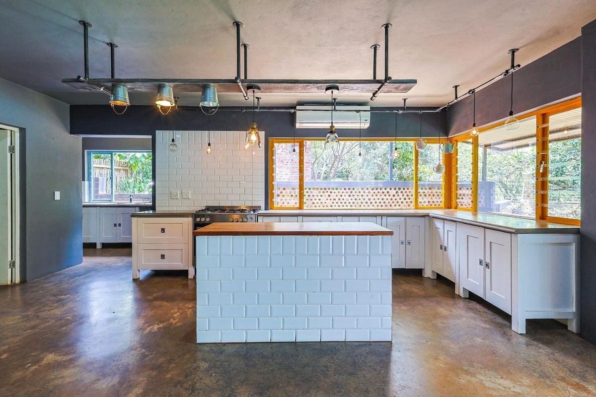 Spacious kitchen featuring a central island, white subway tile backsplash, custom cabinetry, concrete flooring, and industrial-style pendant lighting.