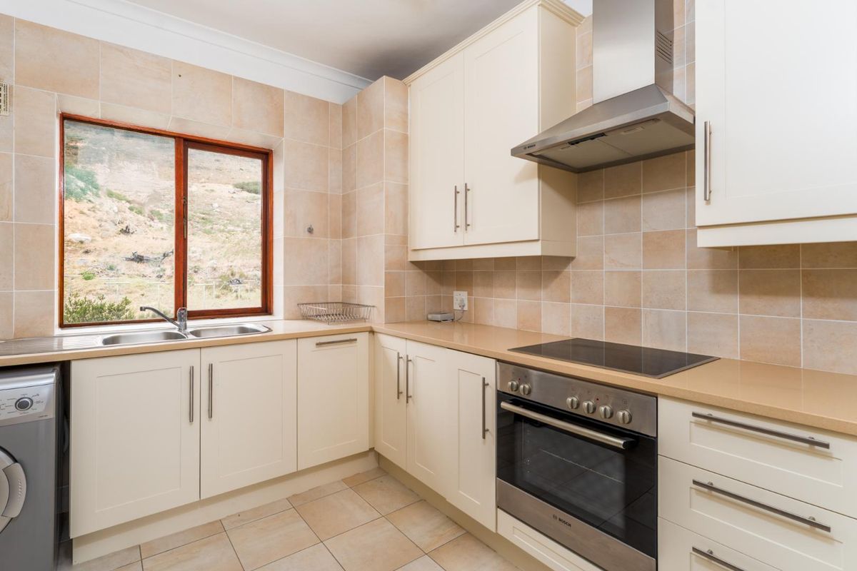 A functional kitchen featuring cream cabinetry, stone-look countertops, tiled splashbacks, a built-in oven with hob, and an integrated extractor fan.