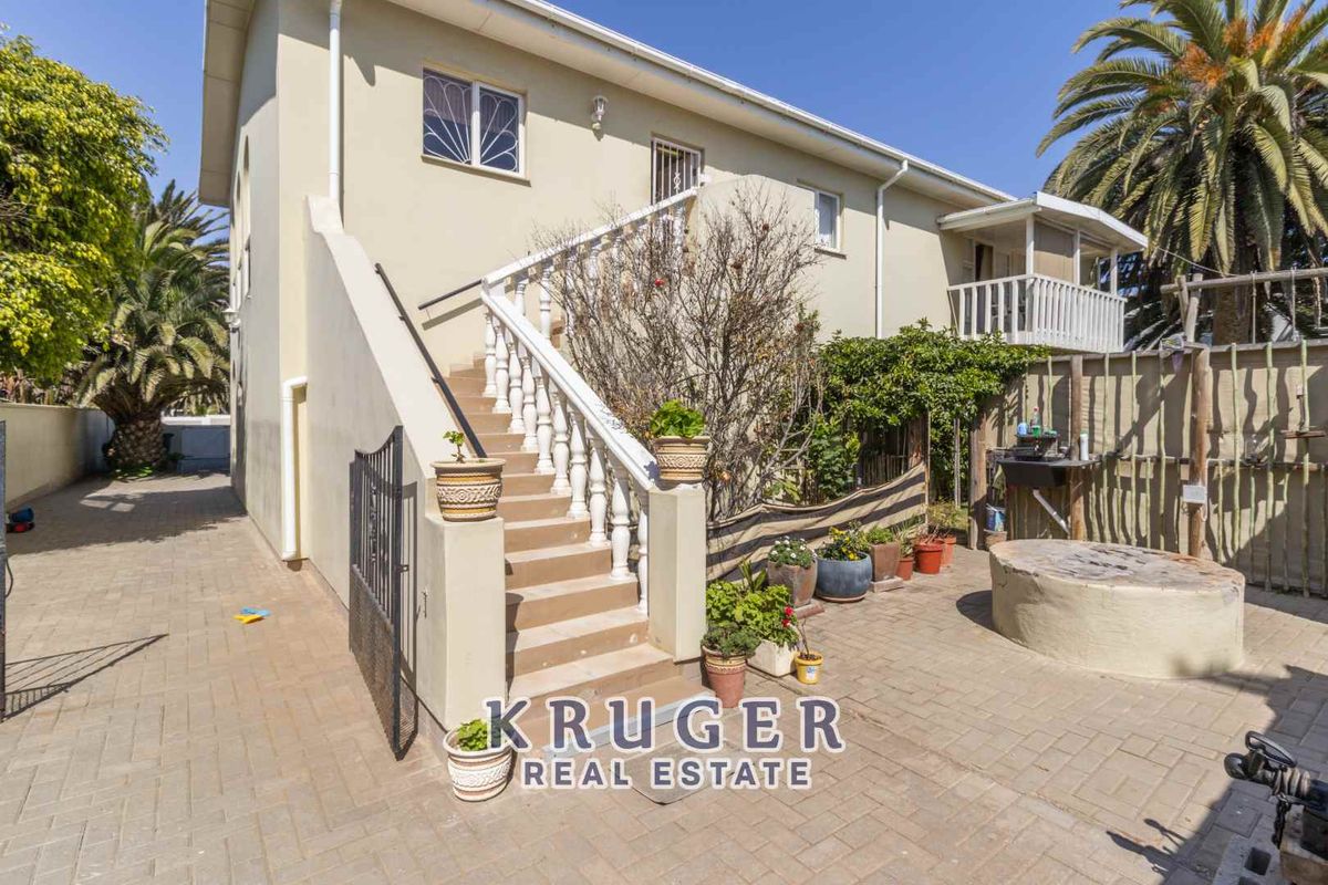 Rear exterior view of the property featuring a paved courtyard, external staircase with balustrades, and access to the upper level.