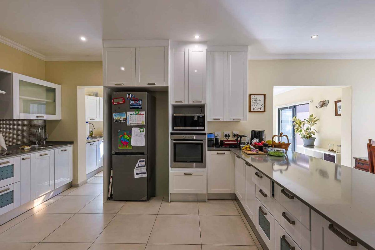 Modern kitchen featuring white cabinetry, stone countertops, built-in oven, microwave, and tiled flooring, with an adjacent scullery area.