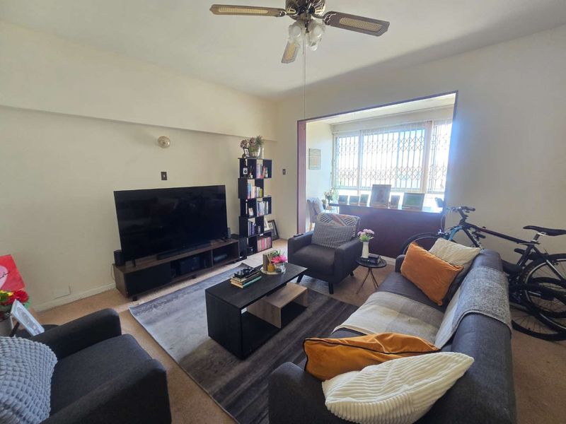 A comfortable living room featuring a ceiling fan and a large window with security gates, providing natural light to the space.
