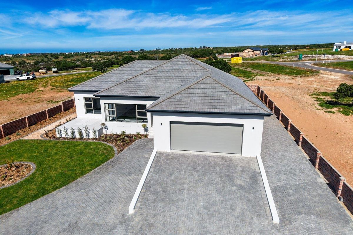 Aerial view of a modern single-story house featuring a tiled roof, paved driveway, double garage, and landscaped garden within a residential estate.