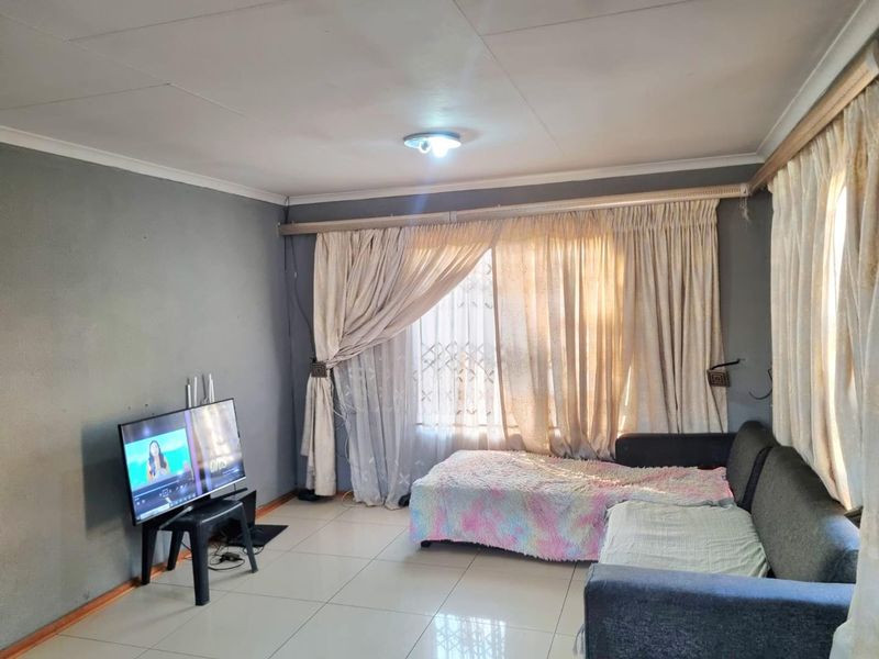 A living room featuring tiled flooring, ceiling cornices, and large windows with security gates, offering a functional space ready for cosmetic updates.