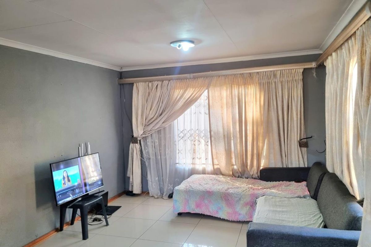 A living room featuring tiled flooring, ceiling cornices, and large windows with security gates, offering a functional space ready for cosmetic updates.