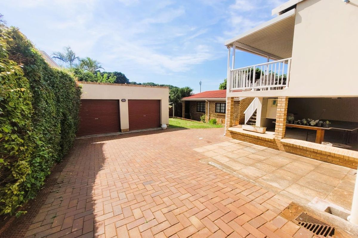 A paved driveway area featuring a double garage, a covered patio space, and an elevated balcony with a white railing.