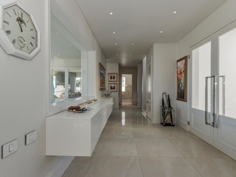 A bright and modern entrance hallway featuring polished porcelain floor tiles, recessed downlighting, and a sleek built-in floating console unit.