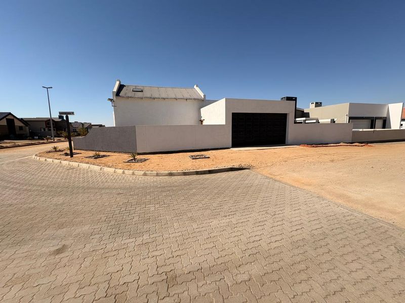 Front exterior view of a modern house featuring a corrugated metal roof, a dark garage door, and a surrounding boundary wall with paved driveway access.