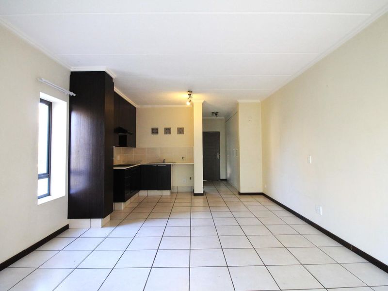 An open-plan living and kitchen area featuring tiled flooring, dark built-in cabinetry, and neutral walls, offering a clean and versatile space.