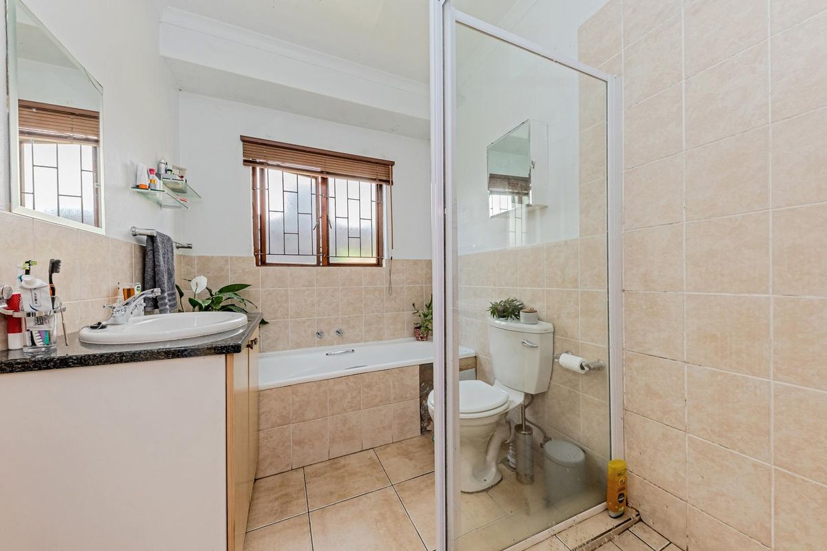 A functional bathroom featuring a built-in bathtub, a separate glass-enclosed shower, a vanity basin, and a toilet with neutral wall and floor tiling.