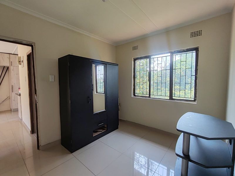 A bedroom featuring tiled flooring, large windows with security bars, and neutral wall tones, offering a functional space with potential for modernization.