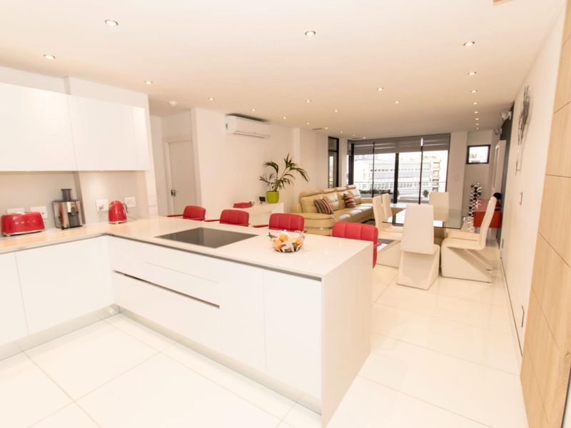 Modern open-plan living area featuring a sleek white kitchen with island, induction hob, and seamless flow to the dining and lounge space.