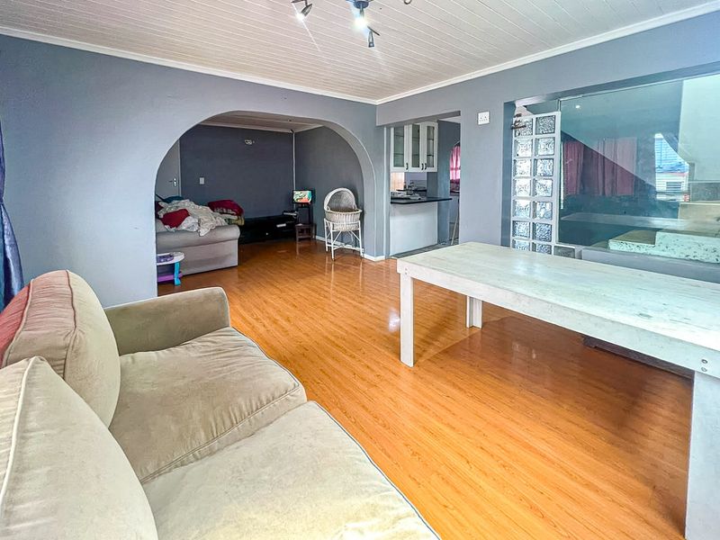 Open plan living and dining area featuring laminate flooring, a distinctive archway, and a glass block partition wall leading to the kitchen space.