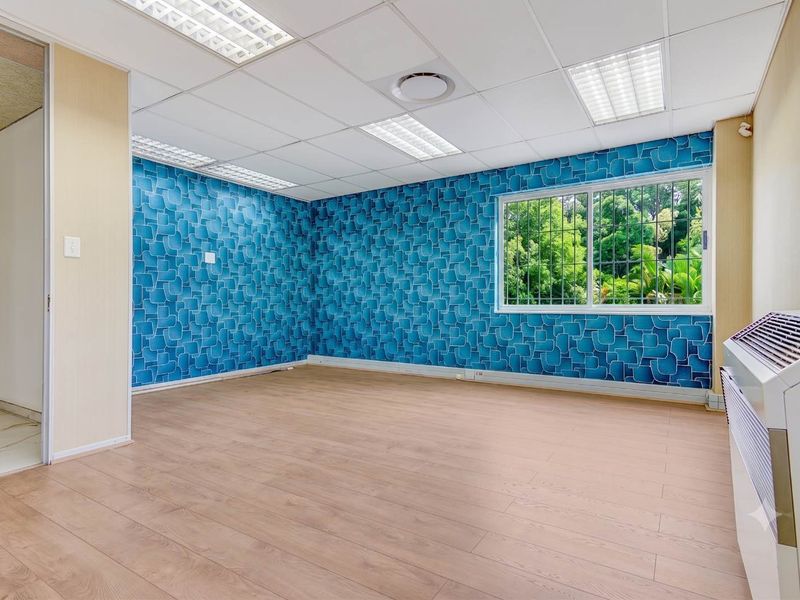 A bright, empty office space featuring laminate flooring, a suspended ceiling with recessed lighting, and a wall-mounted air conditioning unit.