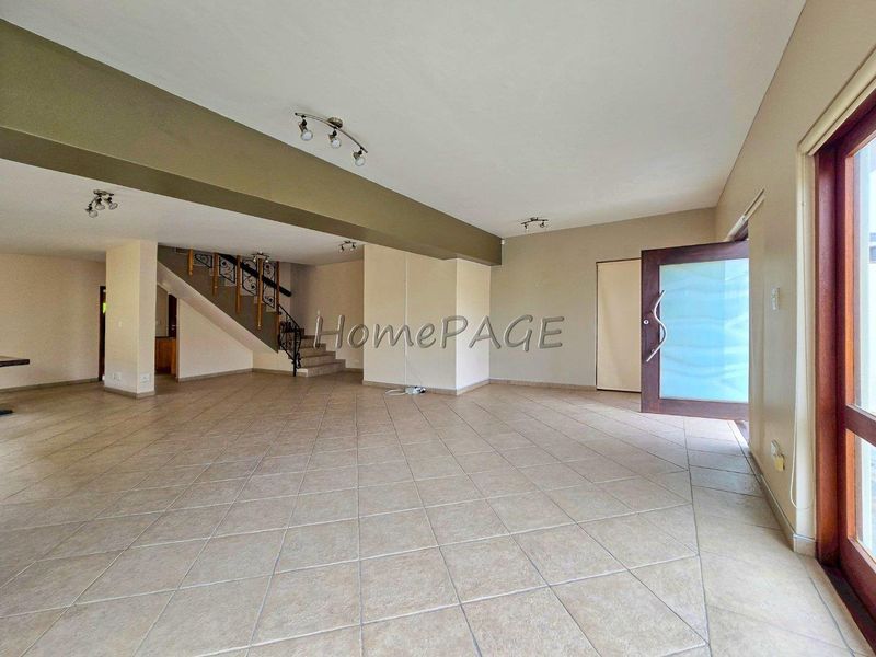 Spacious open-plan living area featuring neutral tiled flooring, a prominent staircase with decorative wrought iron railing, and modern recessed lighting.