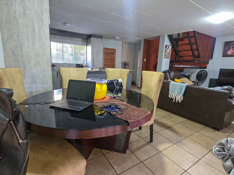 Open-plan living and dining area featuring tiled flooring, a central kitchen island, and a metal staircase leading to the upper level.
