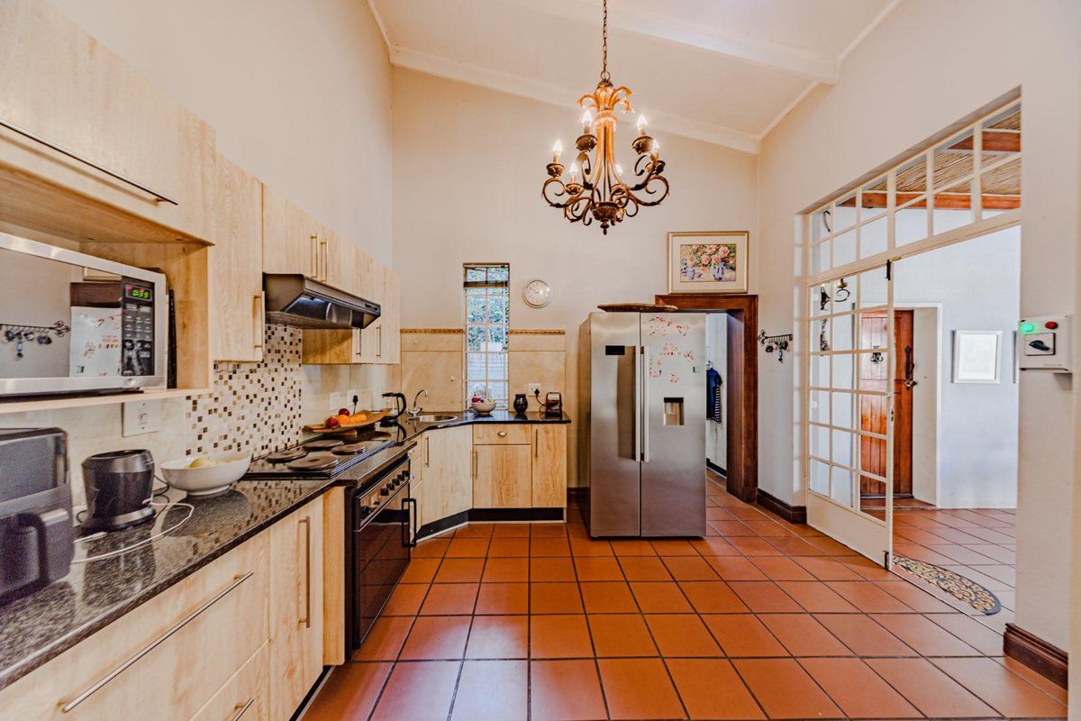 Spacious kitchen featuring light wood cabinetry, granite countertops, terracotta flooring, and a vaulted ceiling with a decorative chandelier.