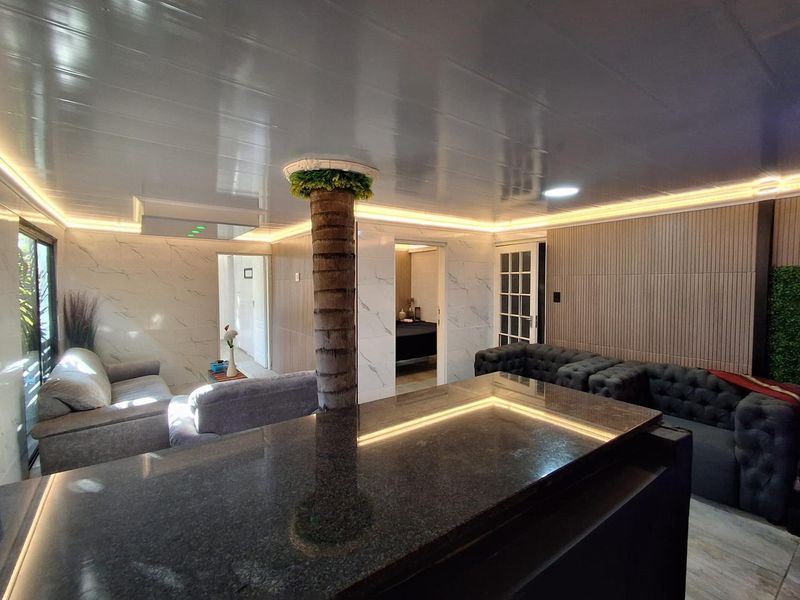 Modern open-plan living area featuring a granite breakfast bar, sophisticated slatted wood wall paneling, marble-look finishes, and integrated ambient LED strip lighting.