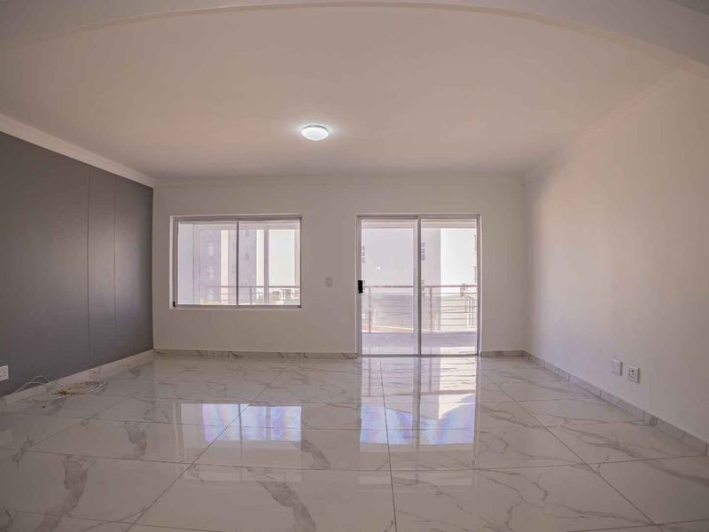 Spacious, bright living area featuring modern marble-look porcelain floor tiles, an accent wall, and direct access to a balcony through sliding glass doors.