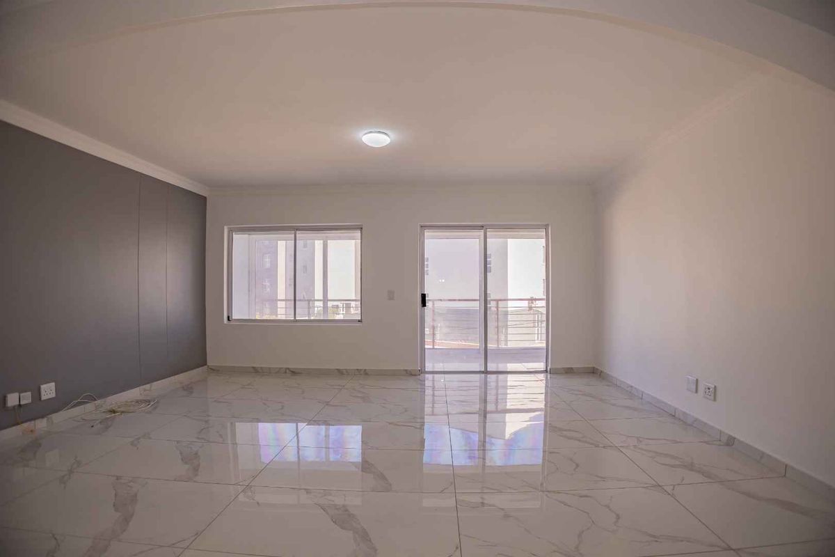 Spacious, bright living area featuring modern marble-look porcelain floor tiles, an accent wall, and direct access to a balcony through sliding glass doors.