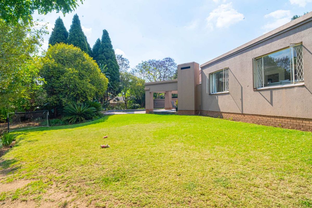 A spacious rear garden featuring a well-maintained lawn, mature trees, and a covered patio area attached to the main house structure.