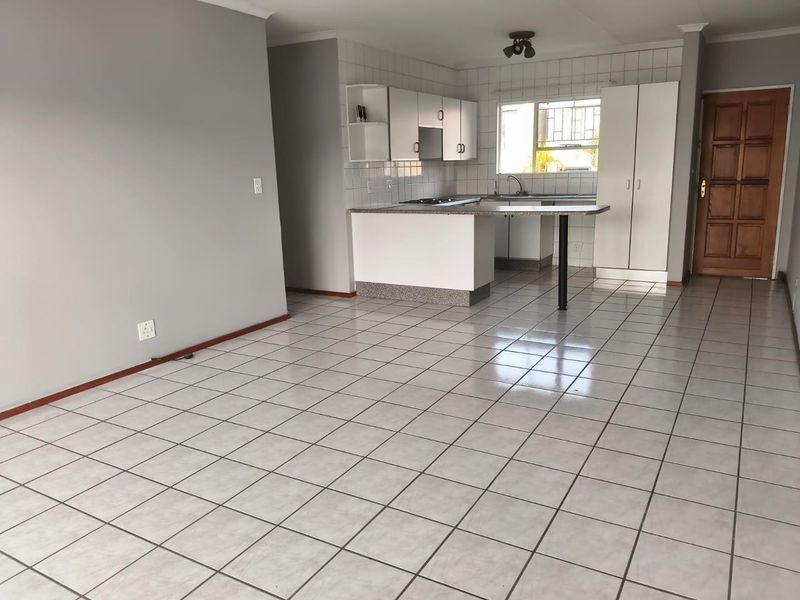 An open-plan living and kitchen area featuring tiled flooring, built-in cabinetry, a breakfast bar, and a functional kitchen layout.