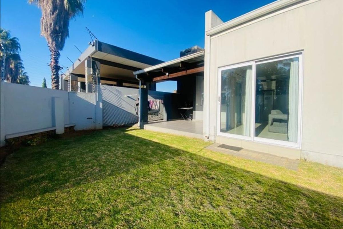 A well-maintained rear garden featuring a covered patio area, paved transition, and a secure perimeter wall.
