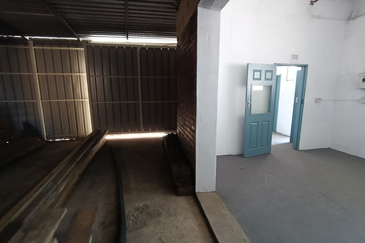 Industrial utility space featuring a combination of covered outdoor storage area and an enclosed room with painted concrete floors and exposed brickwork.