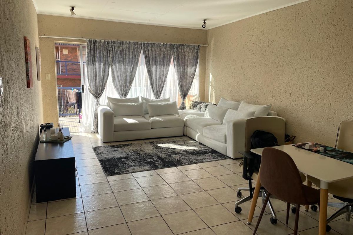 A bright living room featuring tiled flooring, textured walls, and a sliding glass door providing access to an outdoor balcony area.
