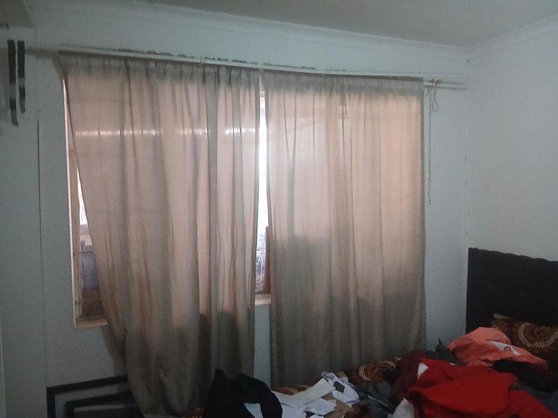 A bedroom featuring a window with security bars and a curtain rod, requiring cosmetic updates to improve the overall finish and appeal.