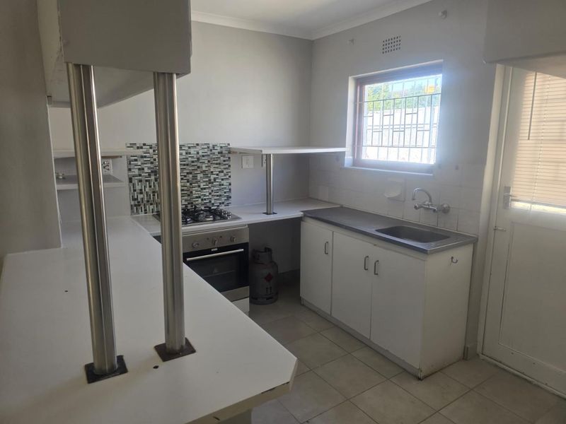 A functional kitchen featuring a gas hob, built-in oven, stainless steel sink, and tiled splashback with ample counter space and storage cabinetry.