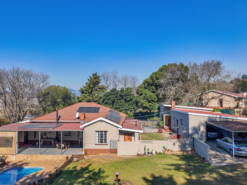 Aerial view of a residential property featuring a main house with solar panels, a swimming pool, covered patio, and a spacious carport.