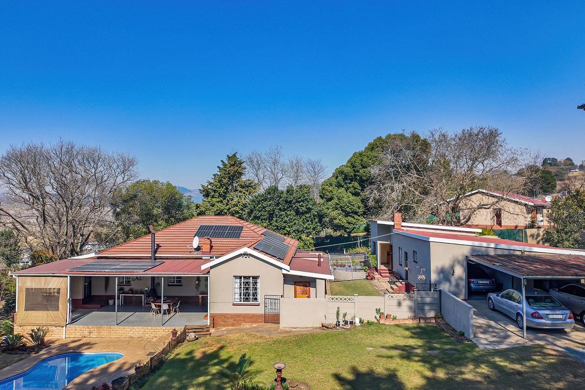 Aerial view of a residential property featuring a main house with solar panels, a swimming pool, covered patio, and a spacious carport.
