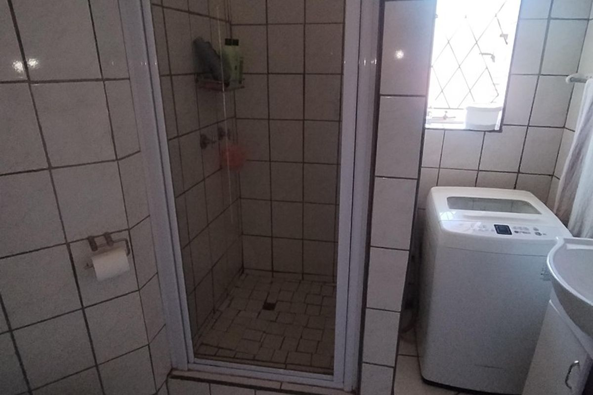 Compact bathroom featuring a shower enclosure, toilet, and vanity basin with tiled finishes throughout.