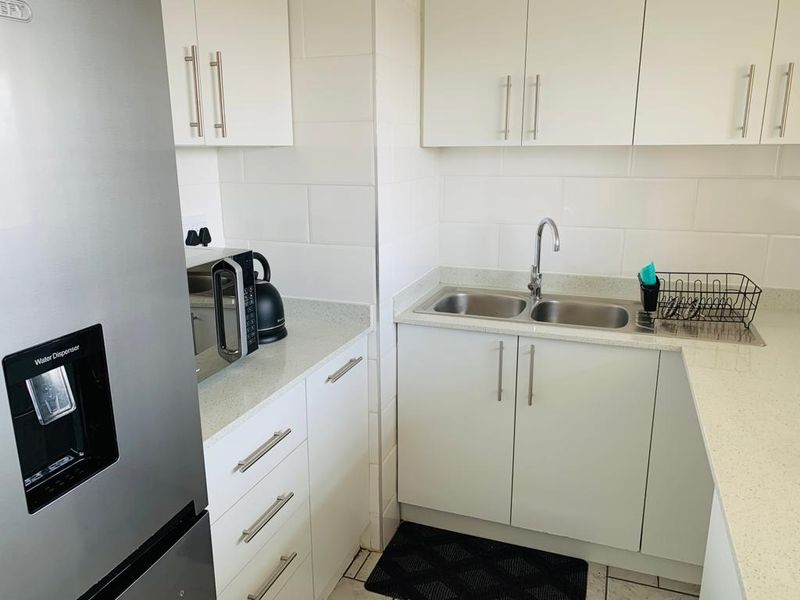 A clean, functional kitchen featuring white cabinetry, stone countertops, a double stainless steel sink, and a tiled backsplash.