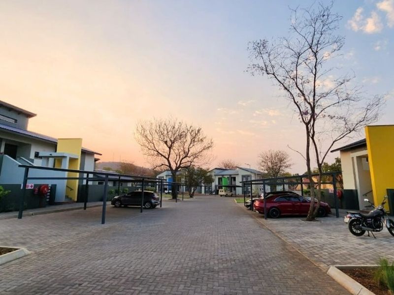 A well-maintained apartment complex exterior featuring paved driveways, covered parking bays, and modern building facades at sunset.