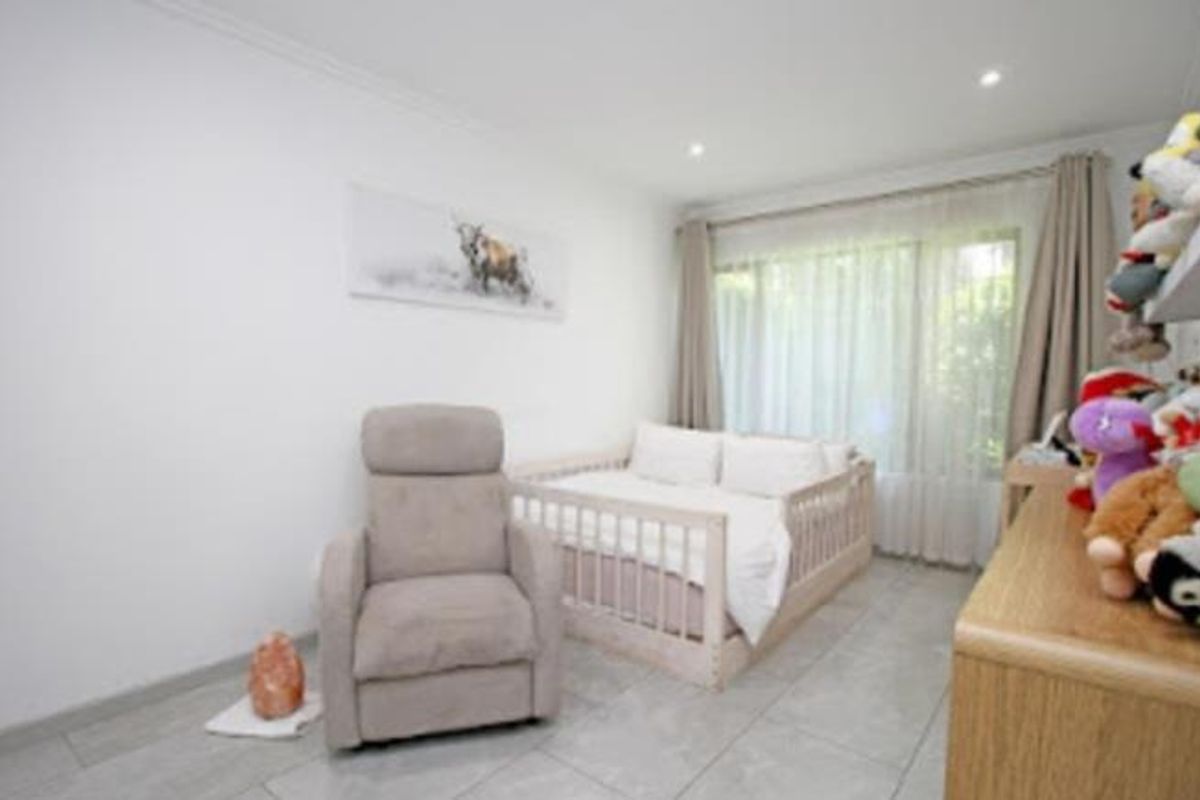 A bright bedroom featuring neutral tiled flooring, recessed ceiling lighting, and large windows with curtains, providing a clean and functional living space.