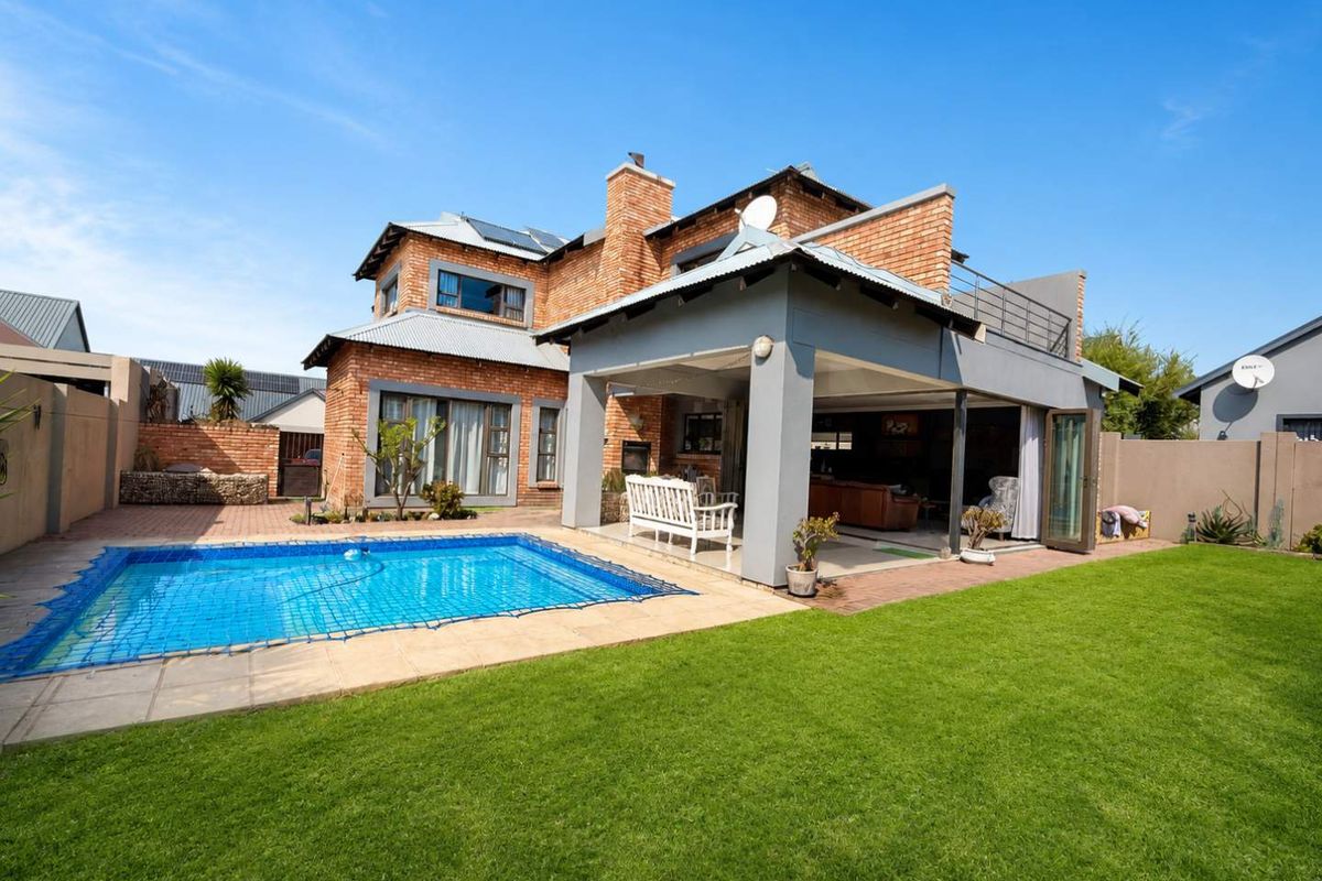 Rear view of a double-story brick house featuring a swimming pool with safety net, a covered patio area, and a well-maintained lawn.