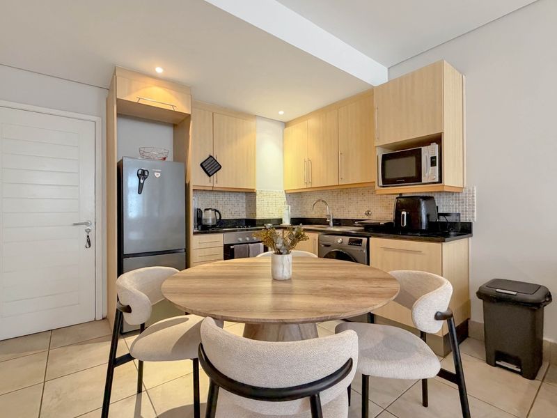 Open-plan kitchen featuring light wood cabinetry, granite countertops, mosaic backsplash, and integrated appliances, seamlessly flowing into the dining area.