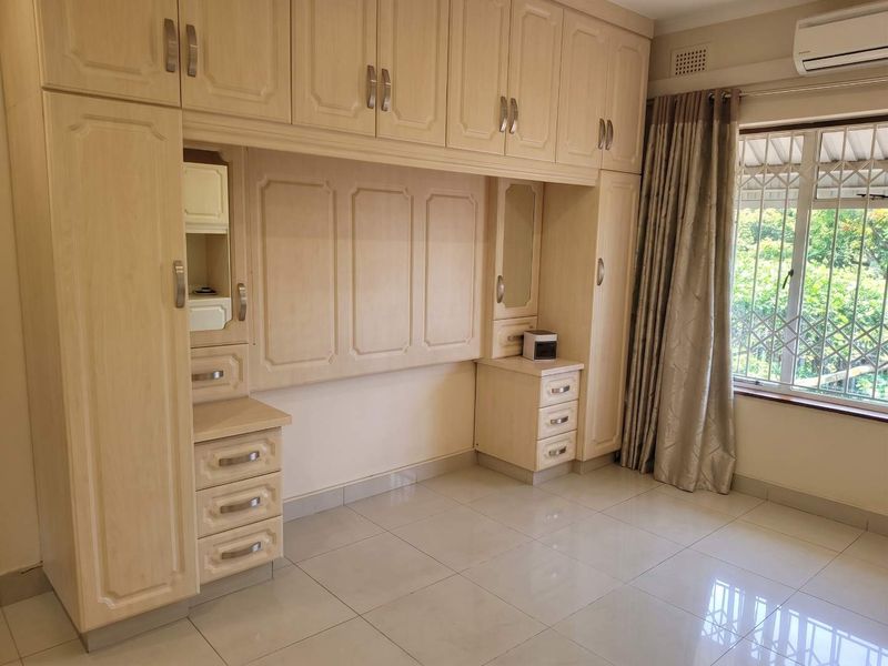 A bright bedroom featuring extensive built-in cabinetry, tiled flooring, and an integrated air conditioning unit, offering ample storage and a clean, functional layout.