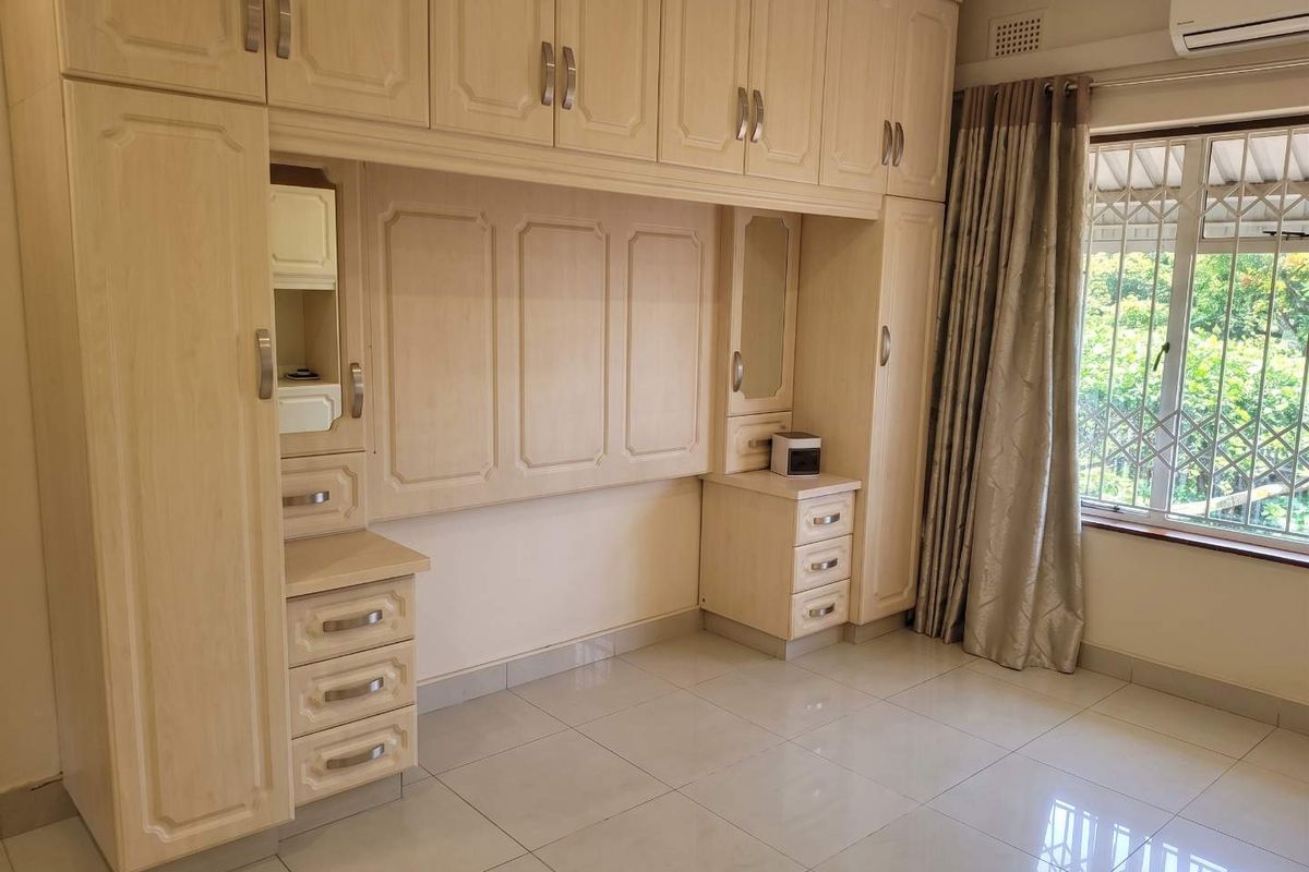 A bright bedroom featuring extensive built-in cabinetry, tiled flooring, and an integrated air conditioning unit, offering ample storage and a clean, functional layout.