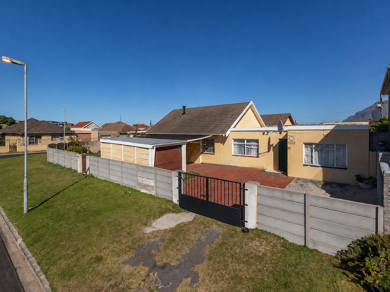 Front elevation of a single-story house featuring a paved driveway, metal gate, precast boundary wall, and a single garage.