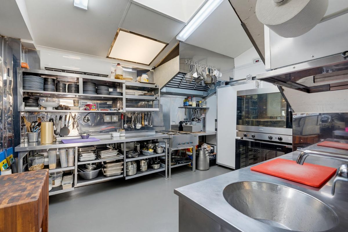 A well-equipped commercial kitchen featuring stainless steel work surfaces, professional-grade extractor hood, built-in oven, and integrated sink, designed for efficient food preparation.