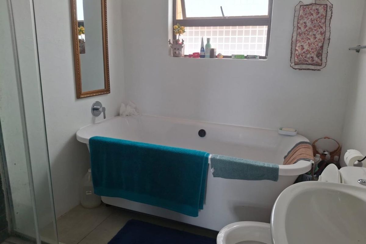 A functional bathroom featuring a freestanding bathtub, a wall-mounted faucet, a pedestal basin, and a shower enclosure with a window for natural light.