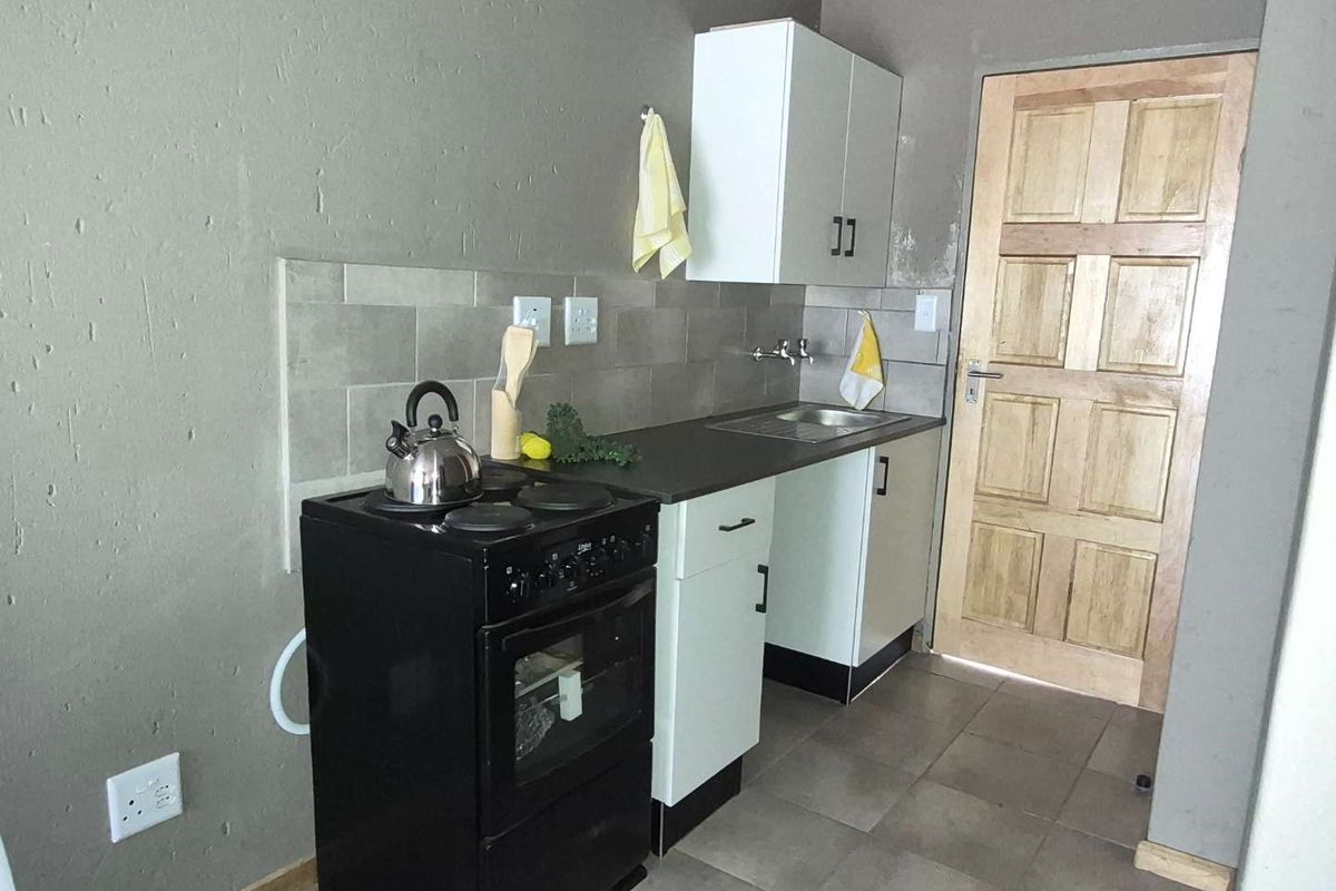 Compact kitchen area featuring built-in cabinetry, a stainless steel sink, tiled backsplash, and a freestanding stove with tiled flooring.