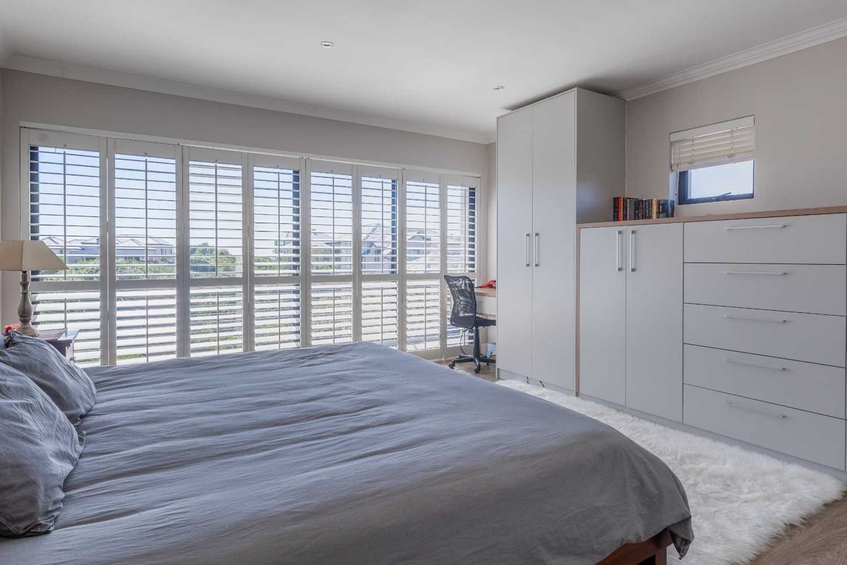 A well-lit bedroom featuring built-in cabinetry, integrated storage, and large plantation shutters that provide ample natural light and privacy.