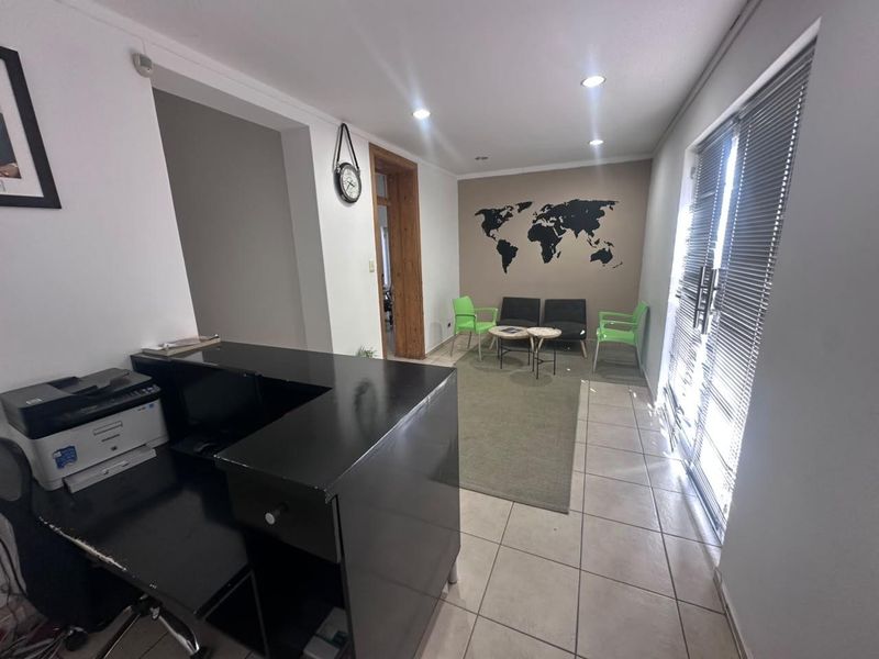 A functional office reception area featuring tiled flooring, recessed lighting, and a built-in reception desk with access to an adjacent waiting area.