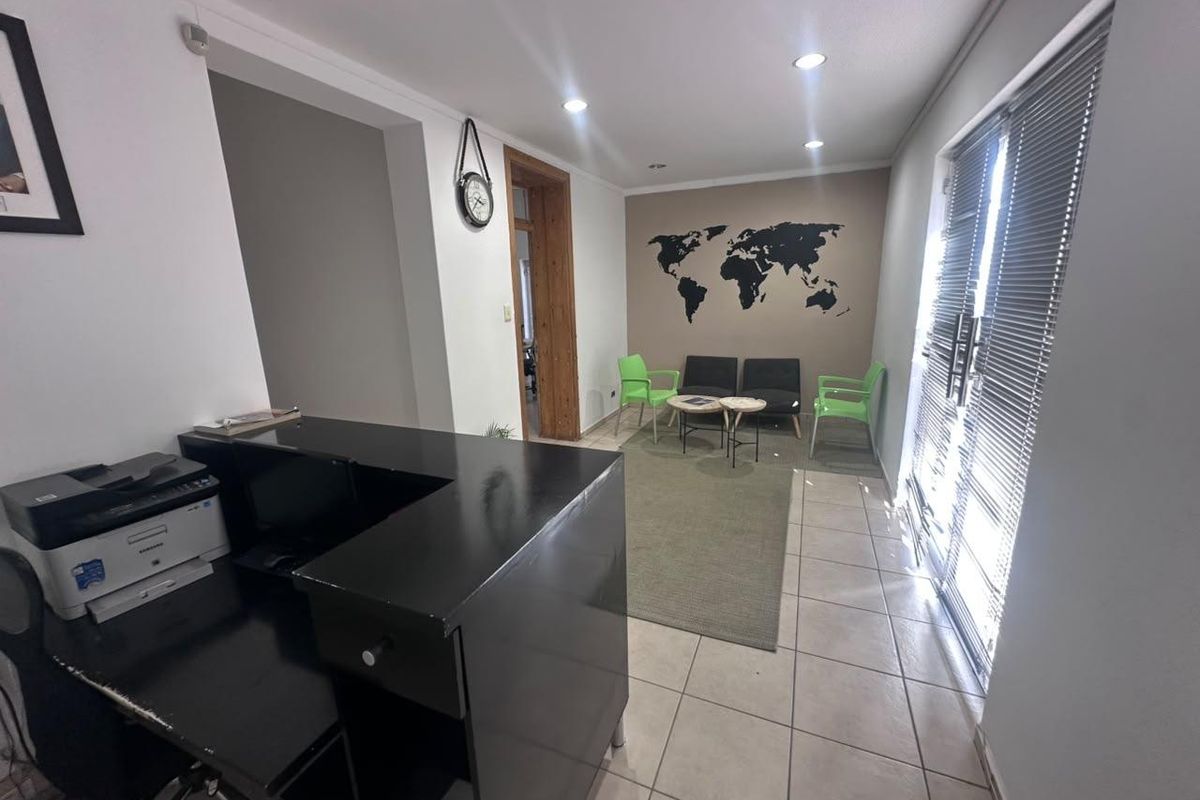 A functional office reception area featuring tiled flooring, recessed lighting, and a built-in reception desk with access to an adjacent waiting area.
