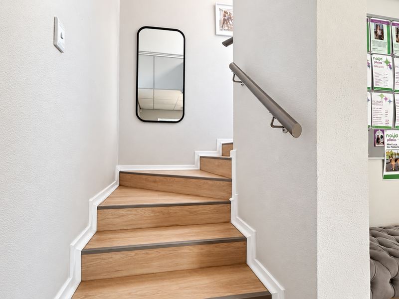 A clean and well-maintained interior hallway featuring a wooden staircase with a modern handrail and white skirting boards.